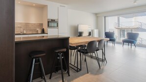 A modern kitchen with a wooden countertop, bar stools, and a dining area with chairs. - Apartment Close to the sea Wall of Mariakerke (Ostend)