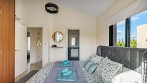 A modern bedroom with a large bed, a view of the outdoors, and a bathroom visible through an open door.