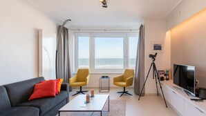 En moderne stue med en grå sofa, to gule lænestole, et sofabord, et fjernsyn og et teleskop.