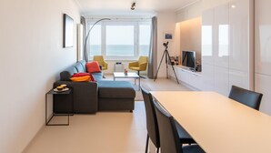 En moderne stue med sofa, stole, spisebord og fjernsyn.
