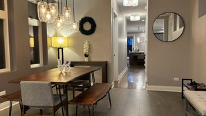 A modern dining area with a wooden table, chairs, and pendant lighting. A decorative wreath and a 'LOVE' sign are on the wall.