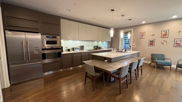 A modern kitchen with stainless steel appliances, a central island with bar stools, and a view of the city through a window.