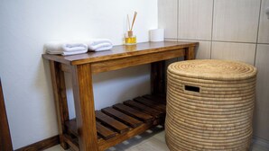 A wooden console table with folded white towels, a small bottle of reed diffuser, and a roll of toilet paper.
