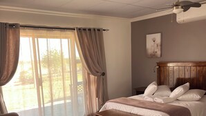 A bedroom with a bed, a wooden headboard, a bedside table, and a view through a large window with curtains.