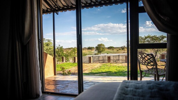 A room with a large sliding glass door leading to an outdoor area with a patio, a chair, and a view of the landscape.