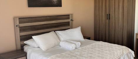 A bedroom with a bed, nightstands, a ceiling fan, a wardrobe, and a wall-mounted picture of a ship at sea.