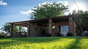 A building with a covered patio, a lawn, and a tree in the background.
