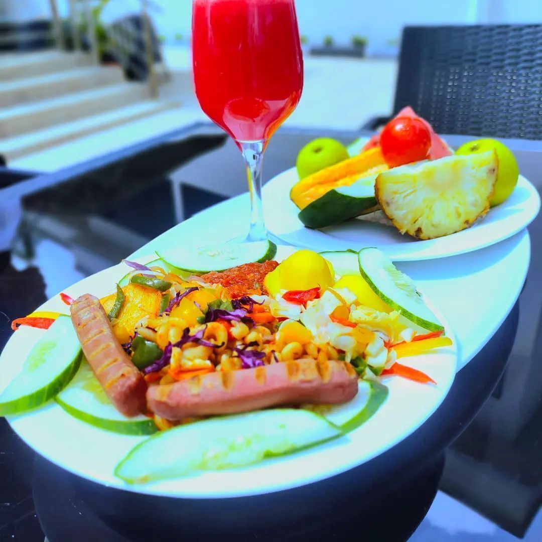 Una comida con varias verduras, un perro caliente y un vaso de bebida roja sobre una mesa.