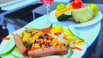 Una comida con varias verduras, un perro caliente y un vaso de bebida roja sobre una mesa.