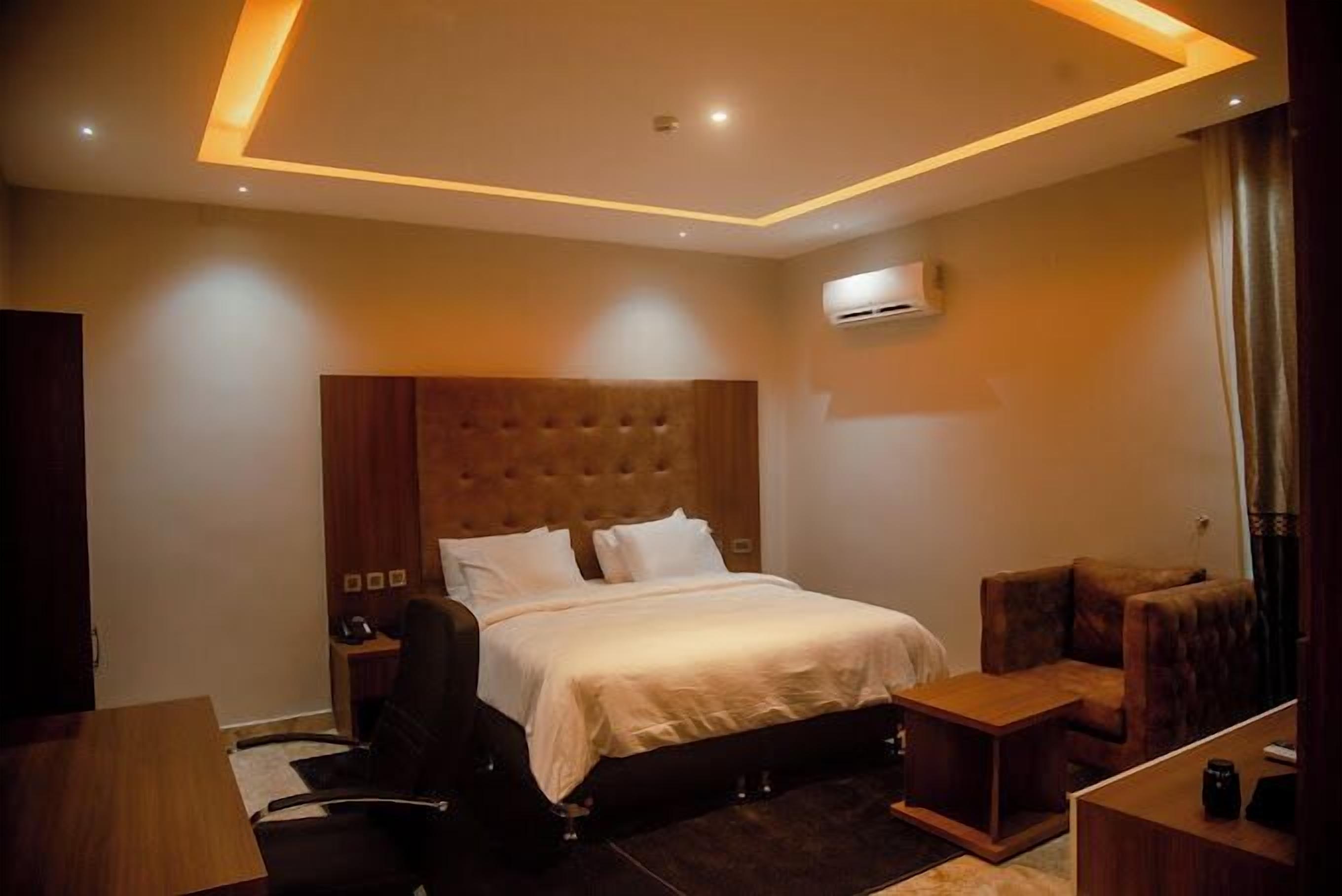 Une chambre d’hôtel moderne avec un grand lit, une tête de lit en bois, un petit bureau, une chaise et une table de chevet.