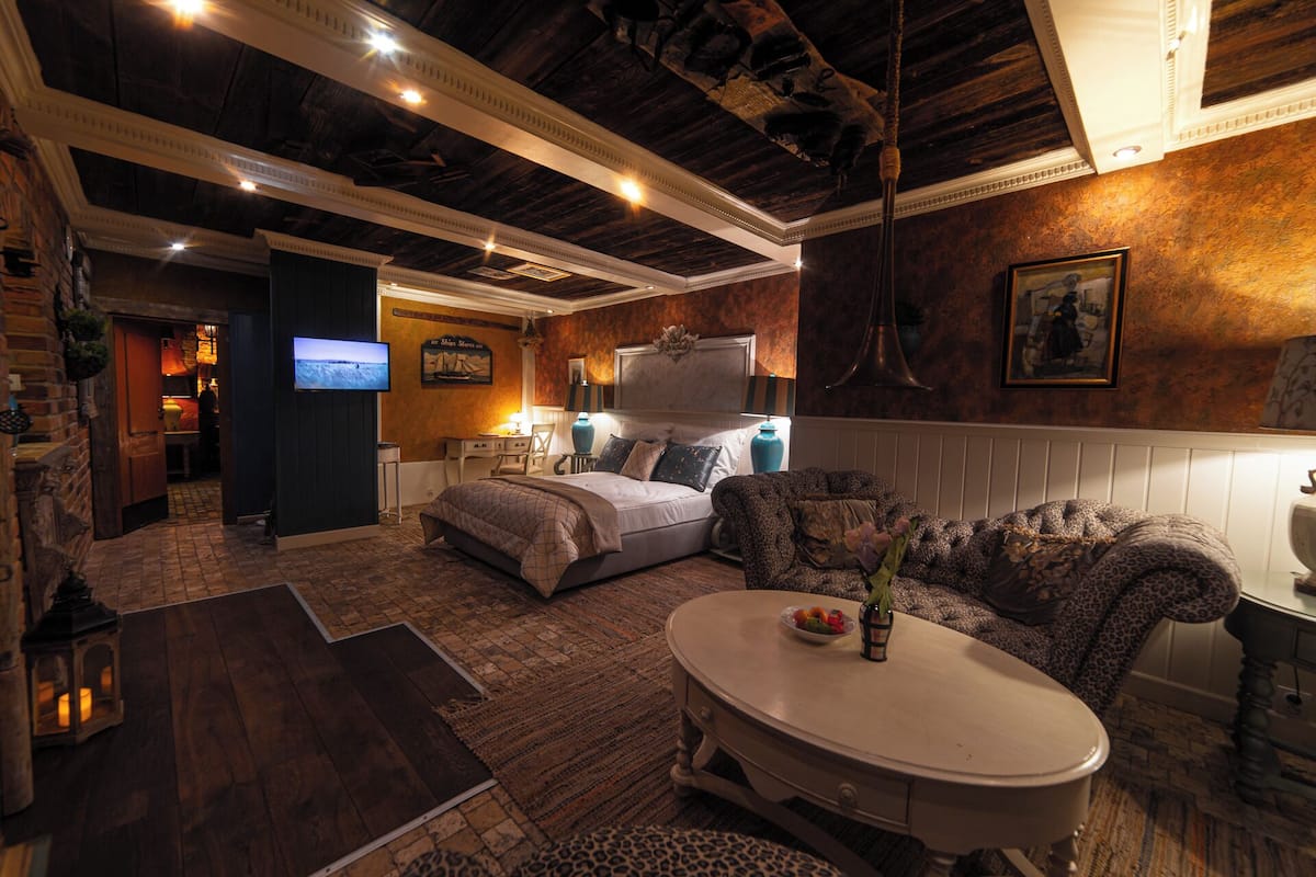 A cozy hotel room with a bed, a sofa, a dining table, and a TV.