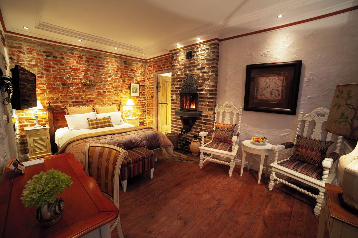 A cozy room with a brick wall, a fireplace, a bed, a chair, and a small table with a plant.