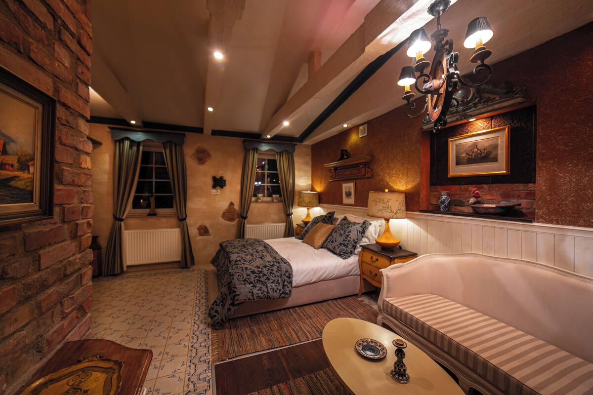 A cozy hotel room with a bed, a sofa, a small table, and a chandelier.