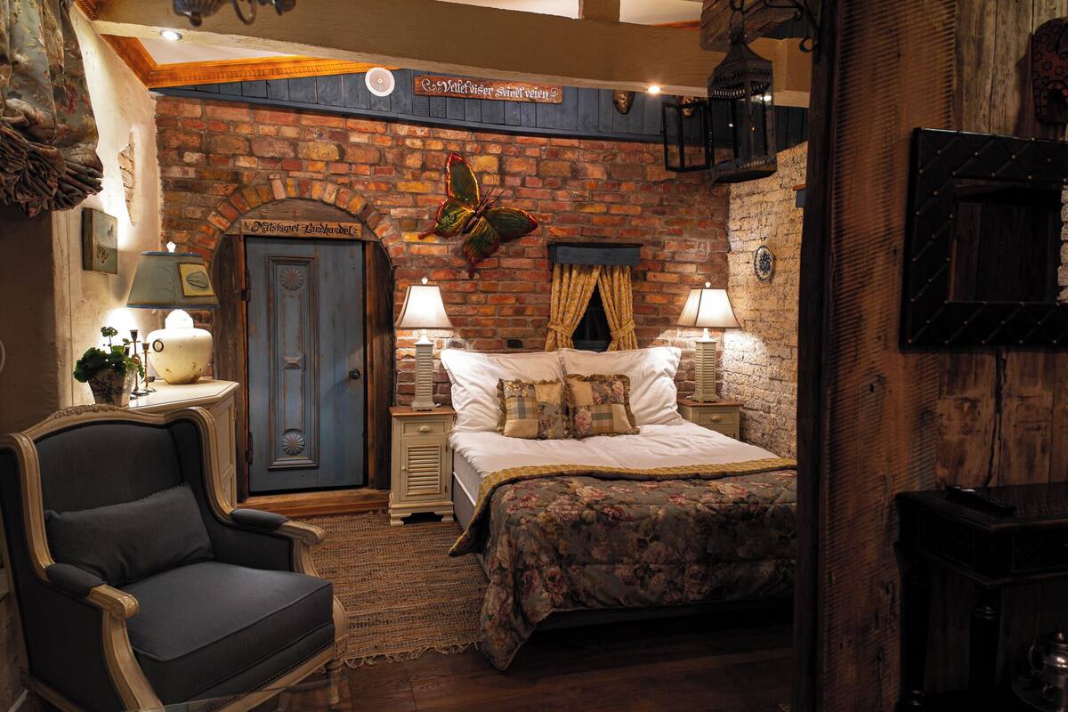 A cozy room with a brick fireplace, a bed with floral bedding, a blue door, and a chair.