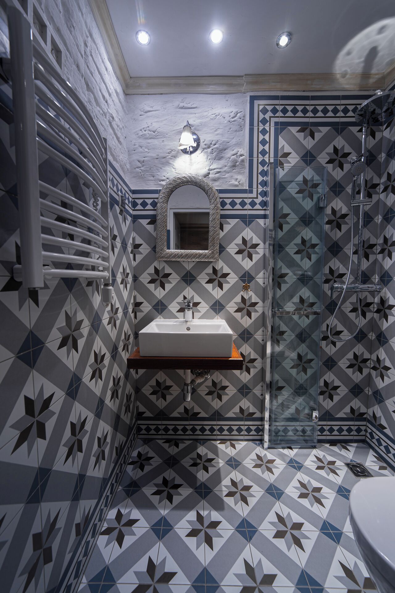 Une salle de bain avec un carrelage aux motifs géométriques, un lavabo blanc, un miroir et un espace douche.