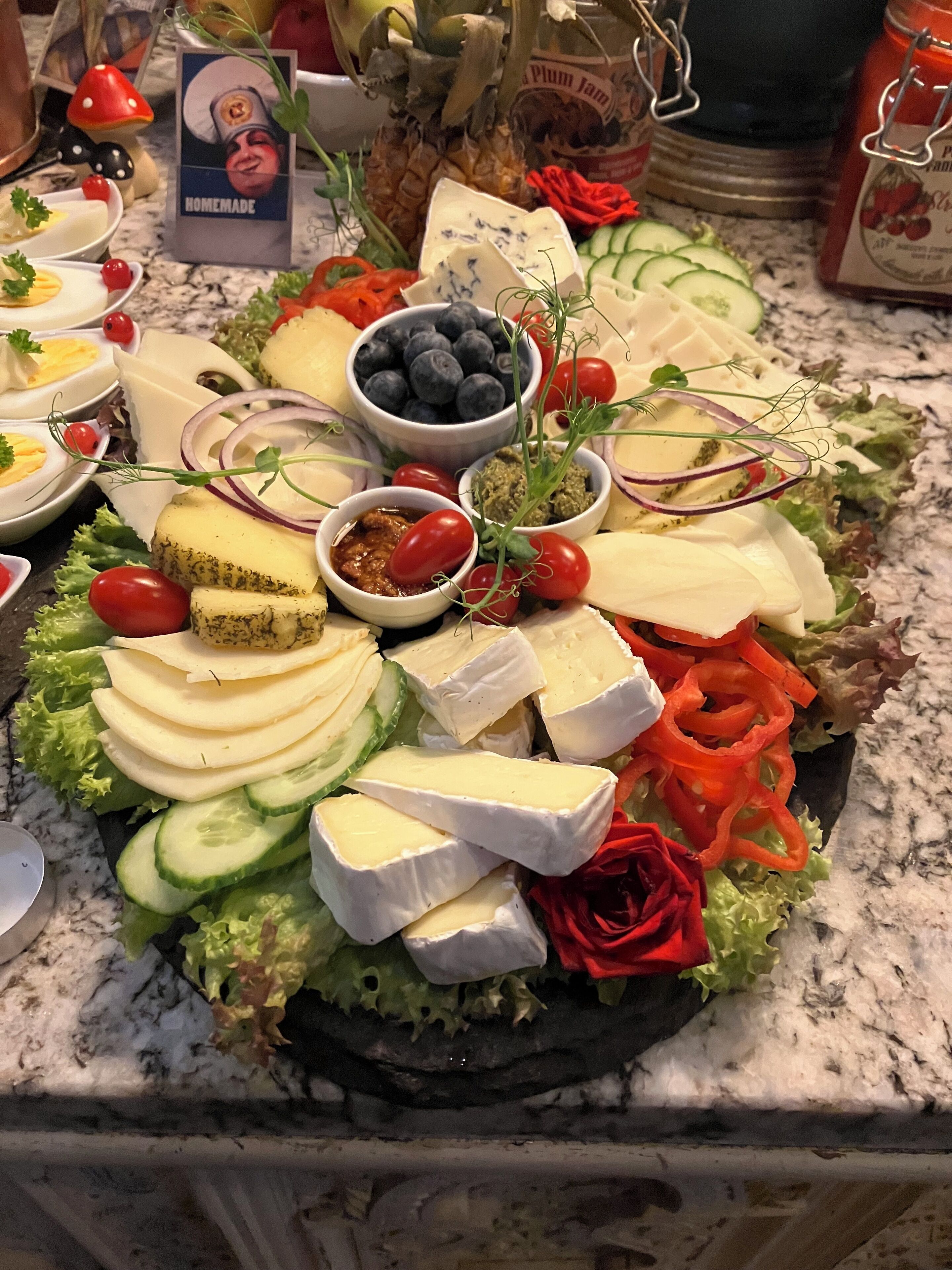 A cheese platter with various cheeses, fruits, and vegetables on a marble countertop.