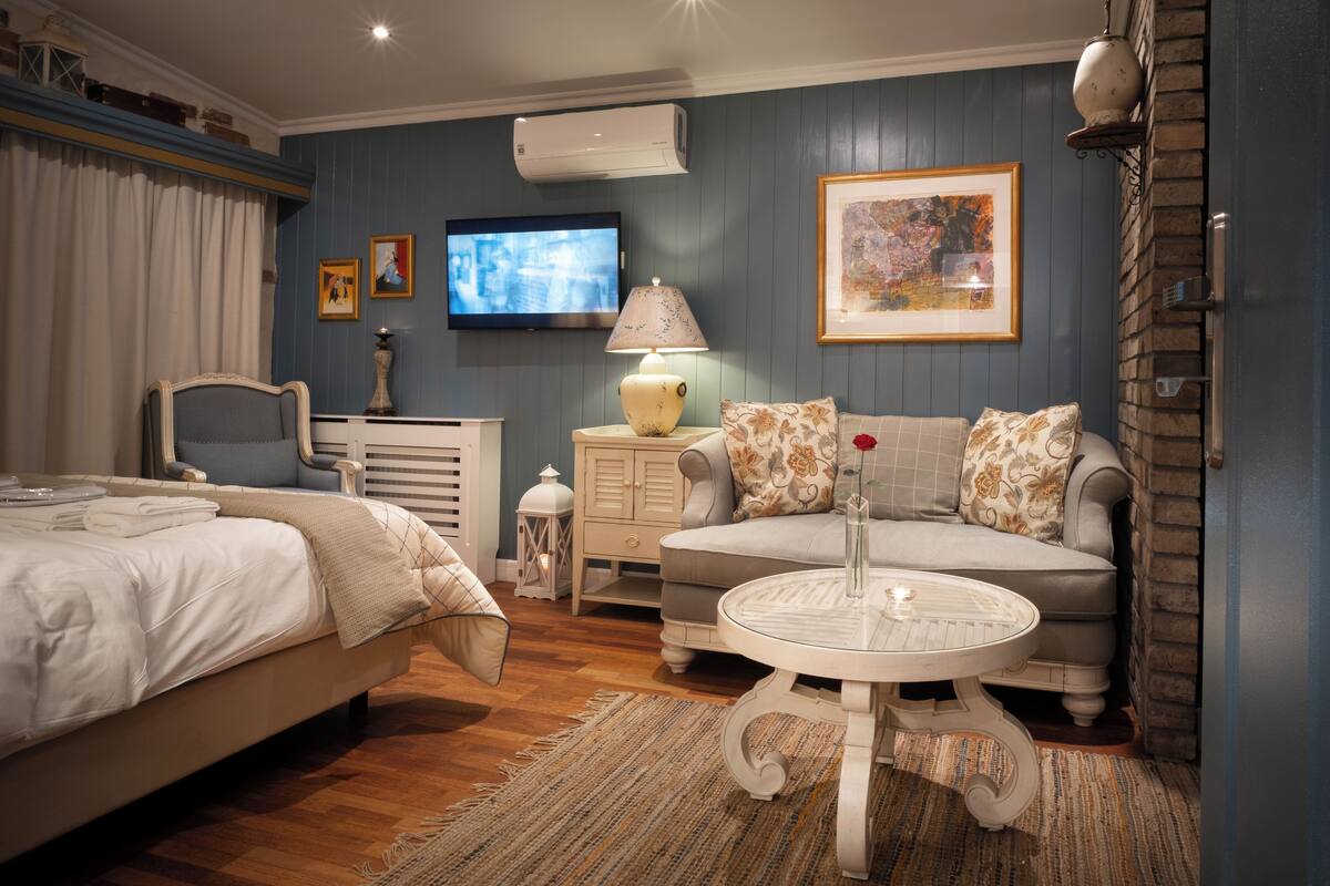 A bedroom with a bed, a sofa, a small round table, a TV, and a wall-mounted air conditioner.