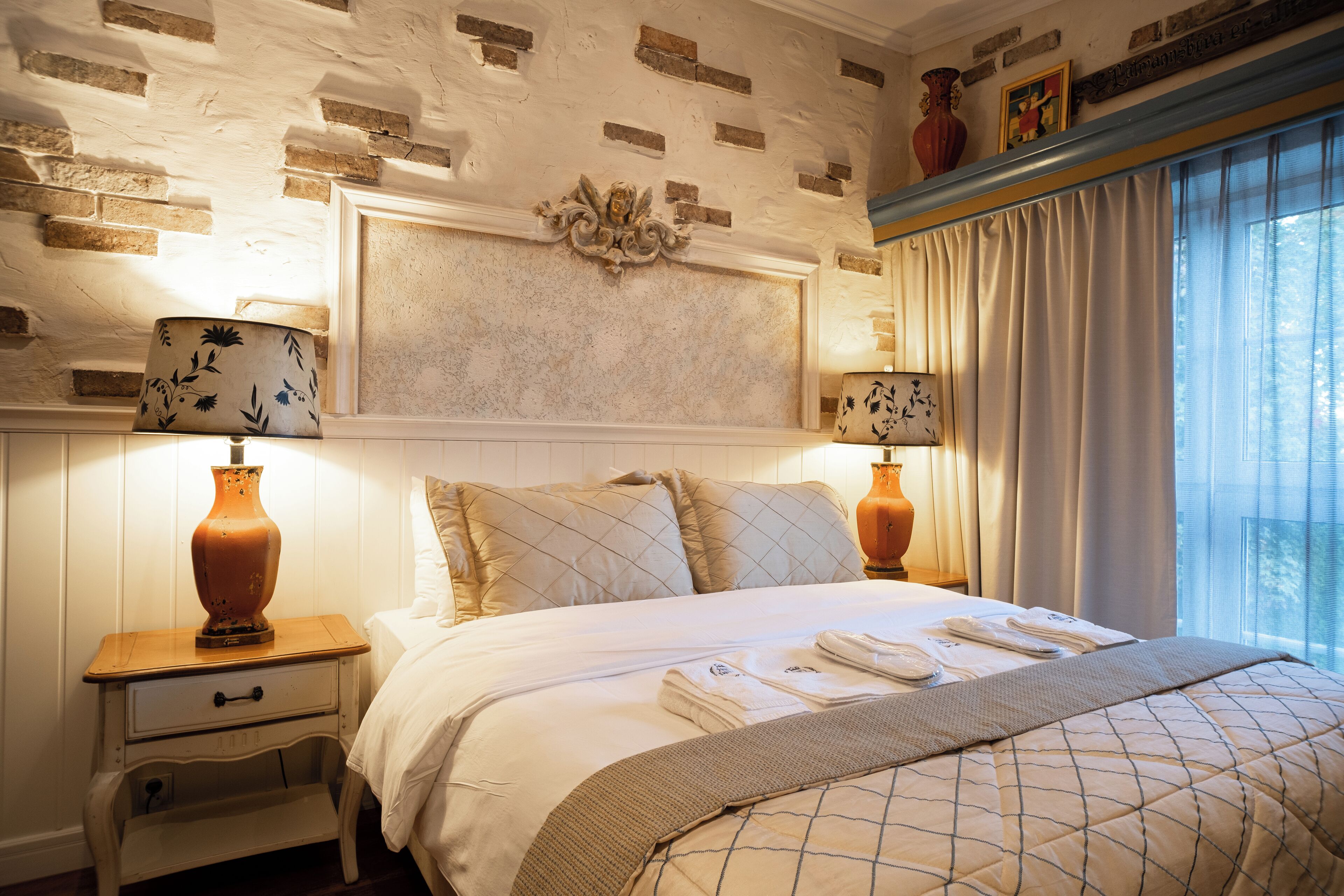 A hotel room with a bed, two bedside lamps, a nightstand, and a window with curtains.