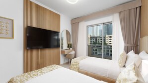 A hotel room with two beds, a TV, a desk, a chair, a window with curtains, and a city view.