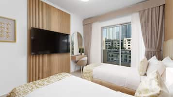 Habitación de hotel con dos camas, televisor, escritorio, silla, ventana con cortinas y vista a la ciudad.