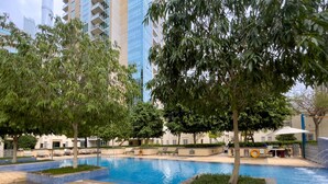 A swimming pool area with tiled flooring, lounge chairs, and trees.
