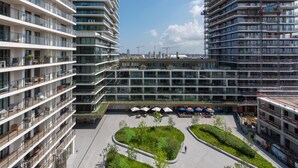 A modern multi-story residential building with balconies, a central courtyard with seating and umbrellas, and a construction site in the background. - Apartment in Ostend With Terrace (Ostend)