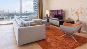 A modern living room with a sofa, armchair, and TV, large windows with a city view, and a decorative vase. - Apartment in Ostend With Terrace (Ostend)