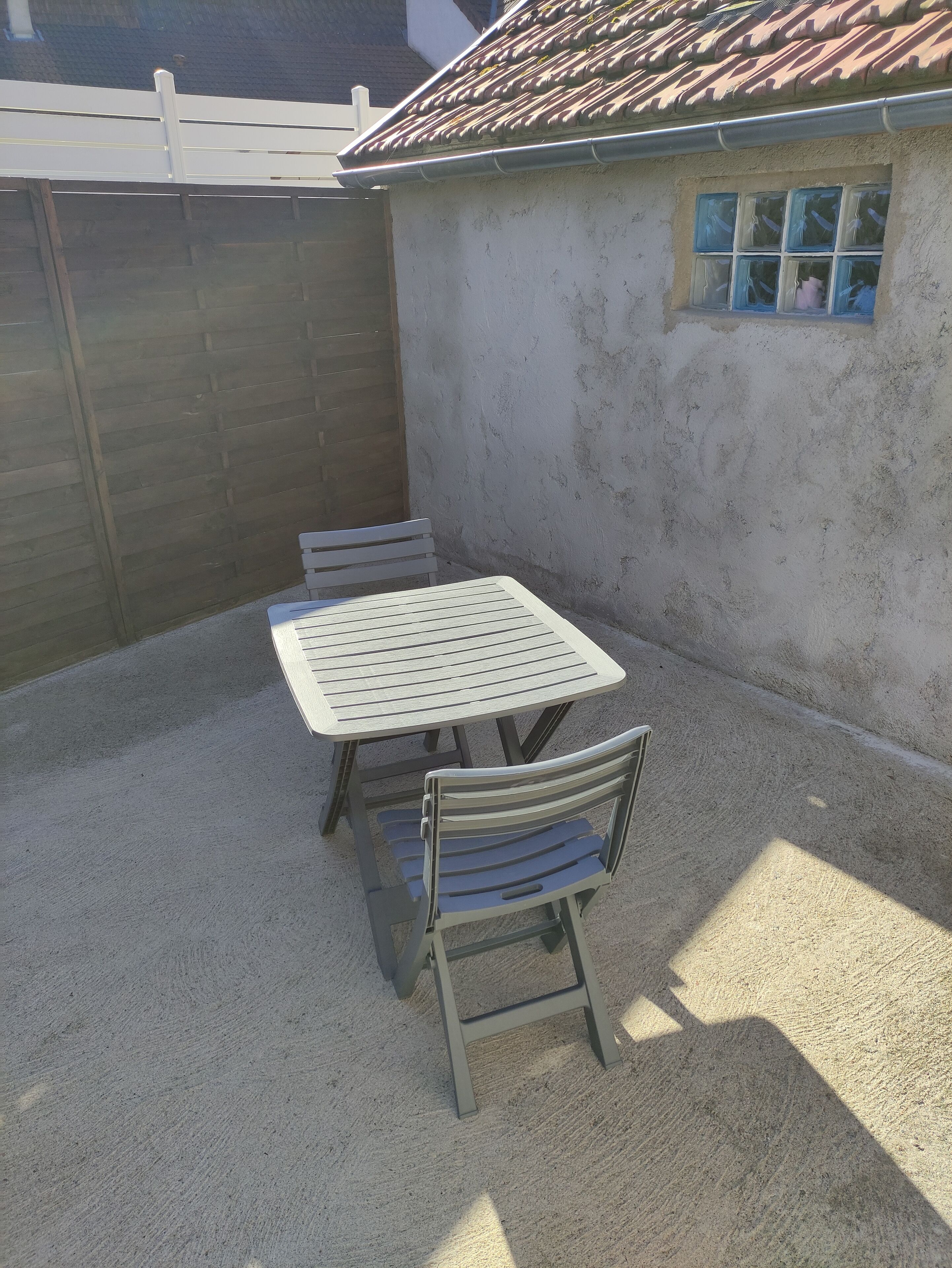 A patio with a table and chairs, a wooden fence, and a building with a tiled roof.