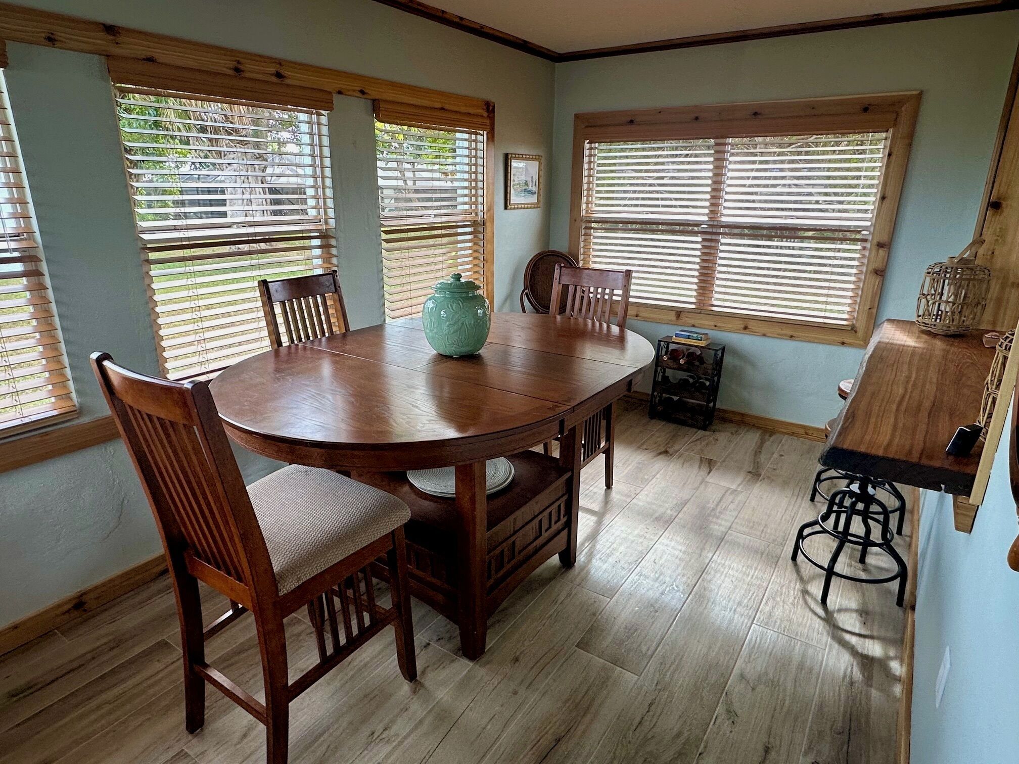 A dining area with a wooden table and chairs, a green vase, and a wooden cabinet with a basket.