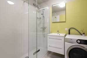 A modern bathroom with a glass shower enclosure, a white sink with a mirror, and a front-loading washing machine. - Apartment in Ostend With Marina Views (Ostend)