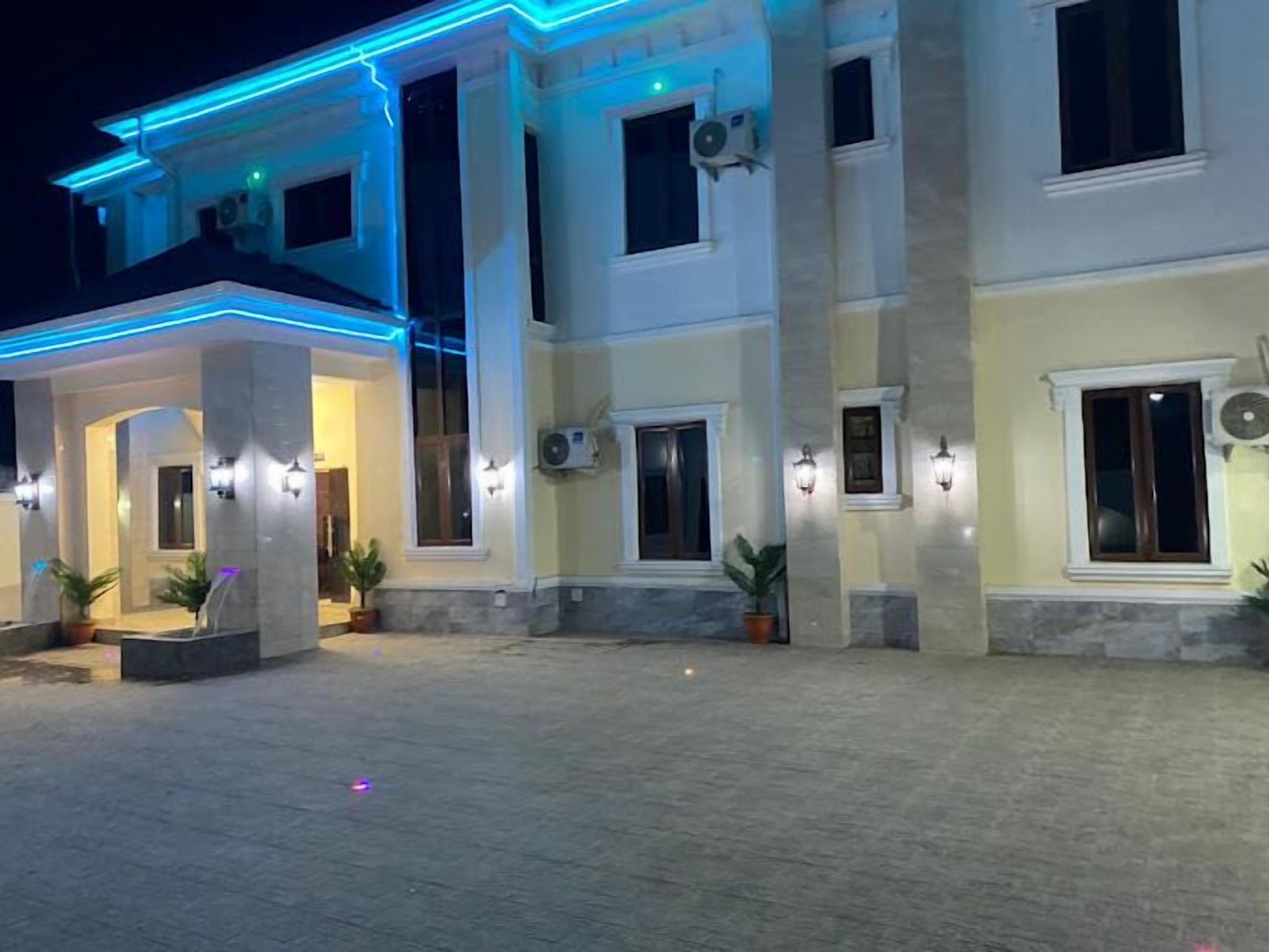 Un edificio de varios pisos con un área de acceso cubierta, iluminación exterior y unidades de aire acondicionado.