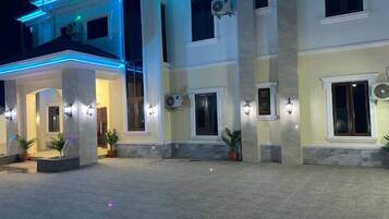 Un edificio de varios pisos con un área de acceso cubierta, iluminación exterior y unidades de aire acondicionado.