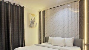A modern hotel room with a large bed, dark curtains, a marble-patterned headboard, and a minimalist decor. - De Vegas Hotel (Nnewi)