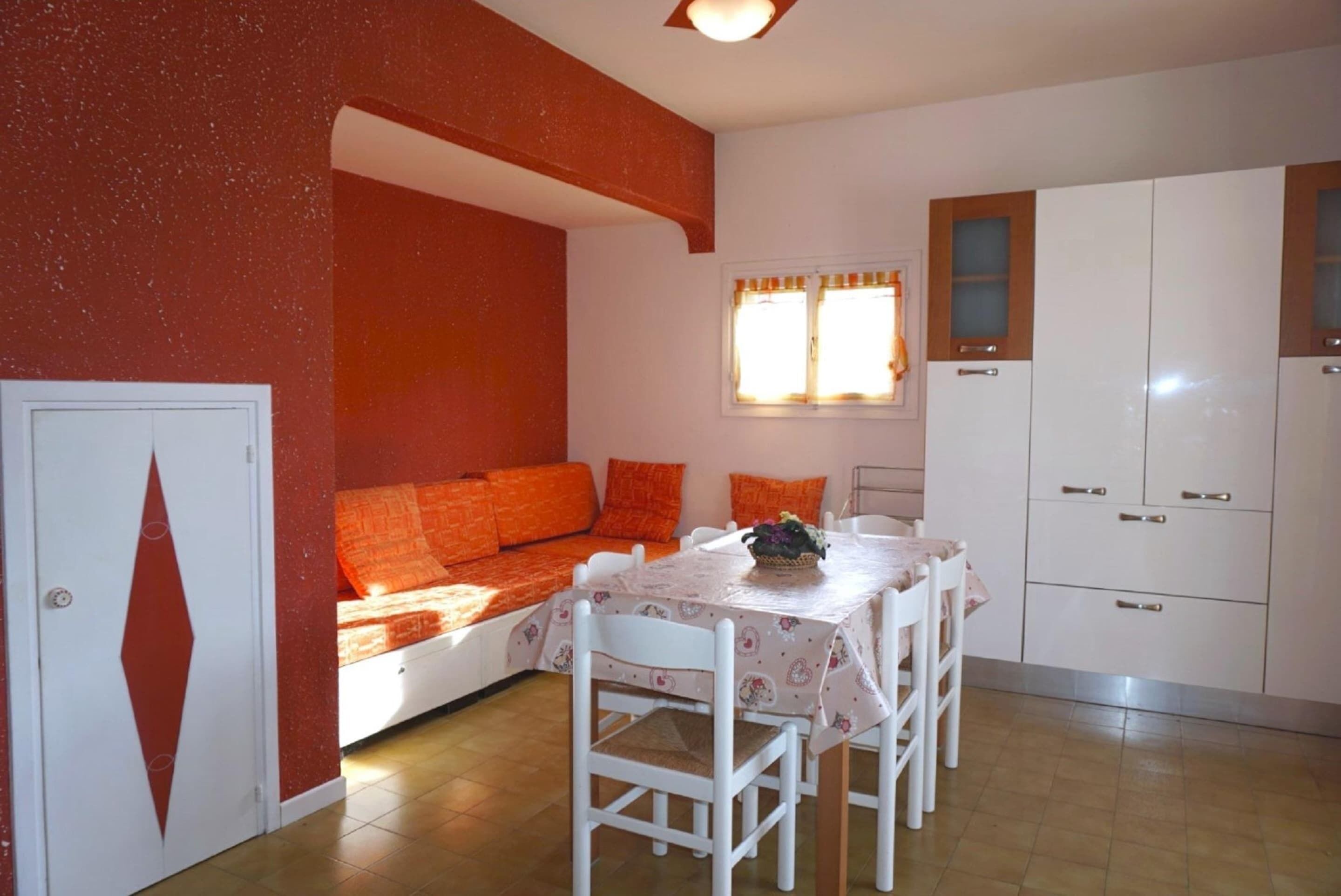 A room with a bed, a dining table with chairs, a window with curtains, and a wardrobe.