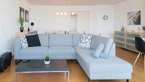 A modern living room with a grey sectional sofa, a black coffee table, and a wooden floor. - Apartment in Ostend Near Shopping Street (Bons Villers)