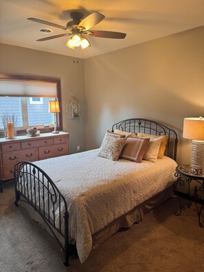 A bedroom with a bed, a dresser, a nightstand, a ceiling fan, and a window with blinds.