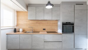 A modern kitchen with grey cabinets, a wooden countertop, a built-in oven, and a pendant light. - Modern Flat Near the sea (Middelkerke)