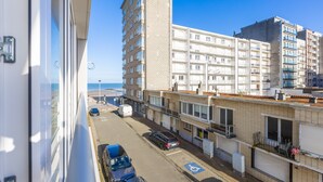 A view of a street with multi-story buildings, parked cars, and a clear sky. - Modern Flat Near the sea (Middelkerke)