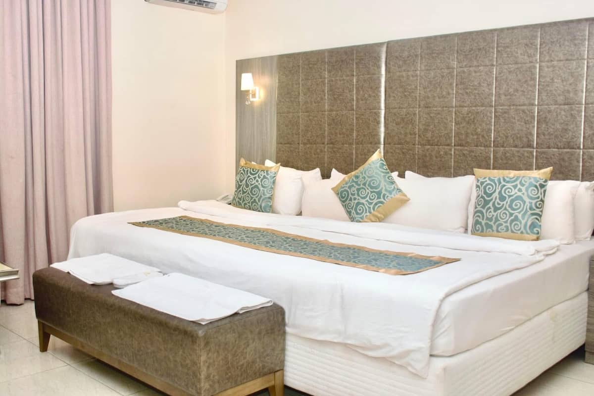 A neatly made bed with patterned pillows, a bedside table with a lamp, and a bench at the foot of the bed.