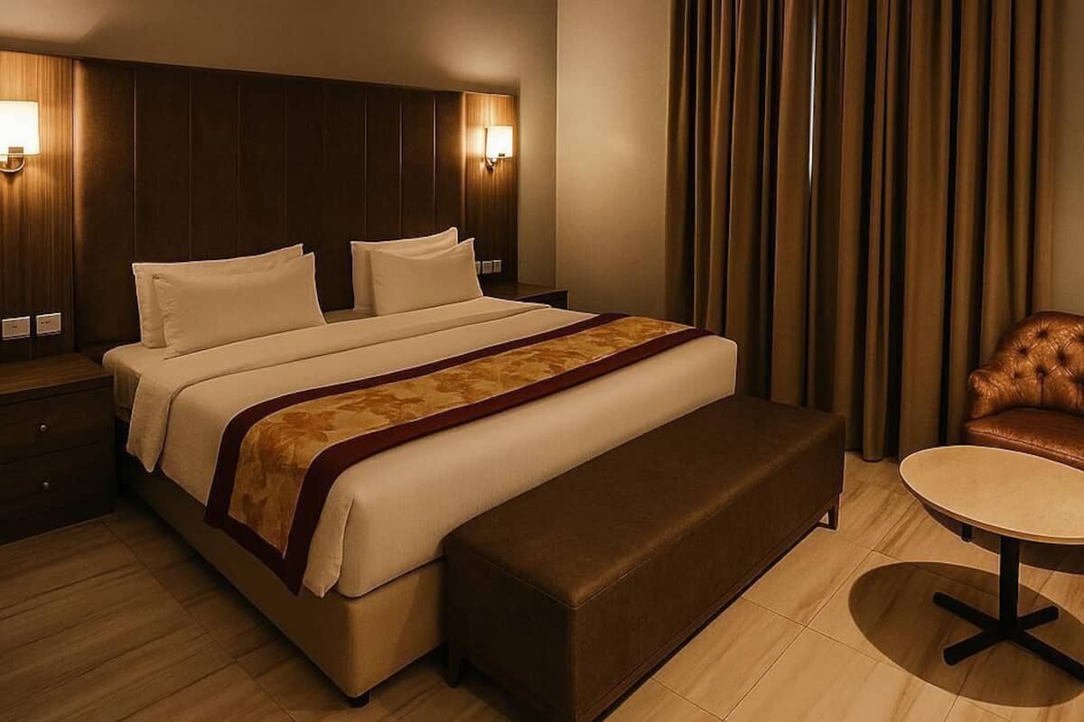 A modern hotel room with a large bed, a bedside table, a small round table, and a leather armchair.
