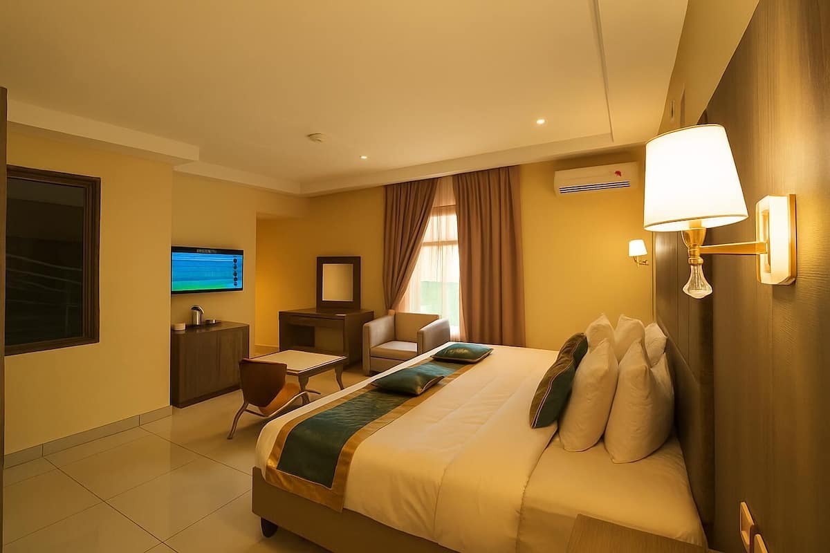 A hotel room with a bed, a desk, a chair, a television, and a wall-mounted lamp.