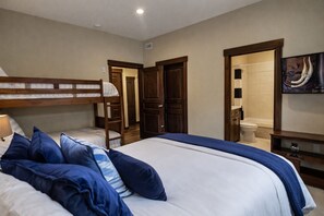 Une chambre avec un lit superposé, un grand lit avec une literie bleue, une armoire en bois, une salle de bain avec des toilettes et un lavabo, et un tableau accroché au mur.