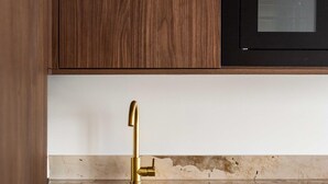 Une cuisine avec des meubles en bois, un robinet doré, un plan de travail blanc et un micro-ondes noir.