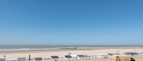 A beachside parking area with a white car and a Dovy van, solar panels, and a clear blue sky.