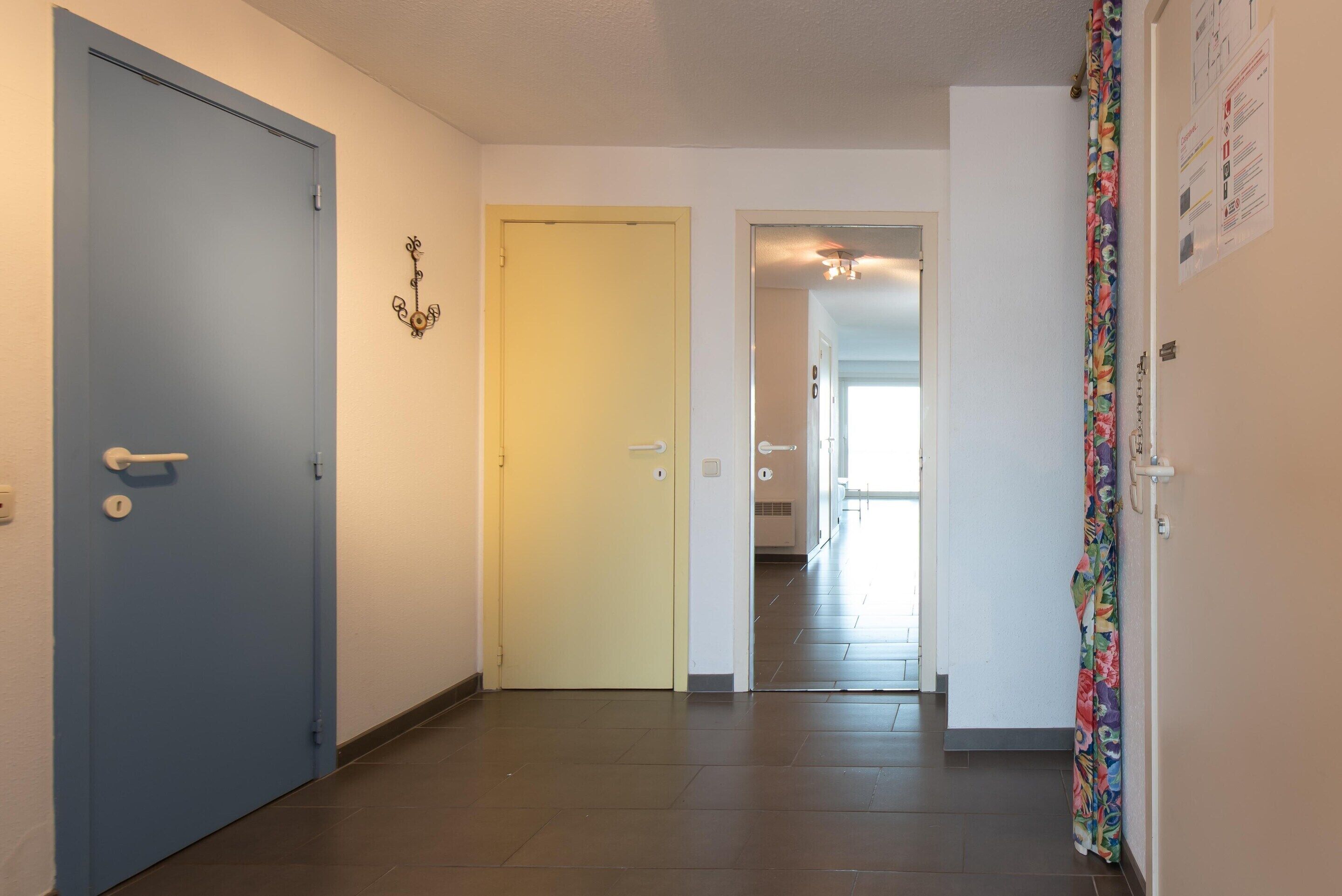 A hallway with a blue door on the left, a yellow door in the center, and a colorful curtain on the right.