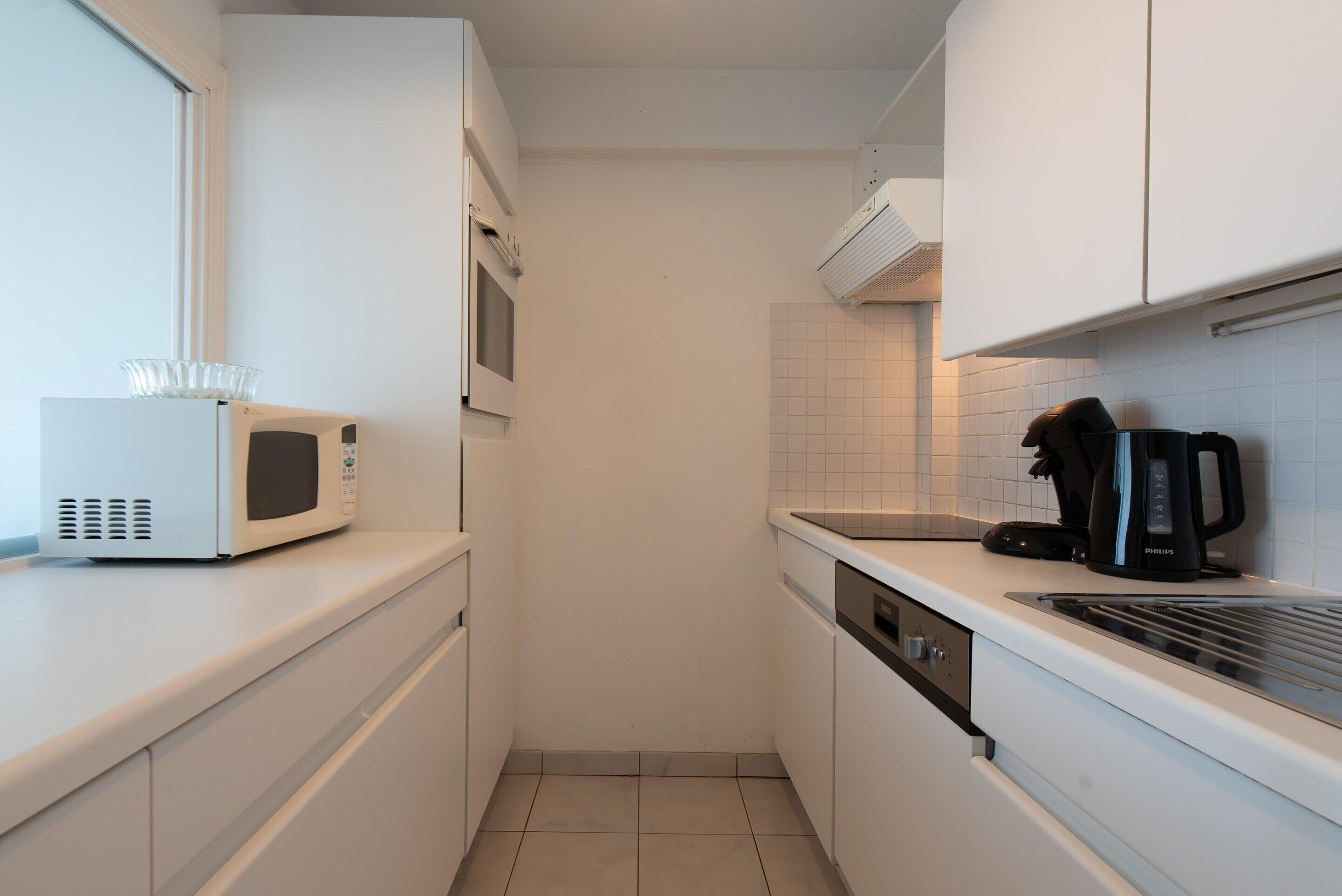 A narrow kitchen with white cabinets, a microwave, a coffee maker, and a dishwasher.