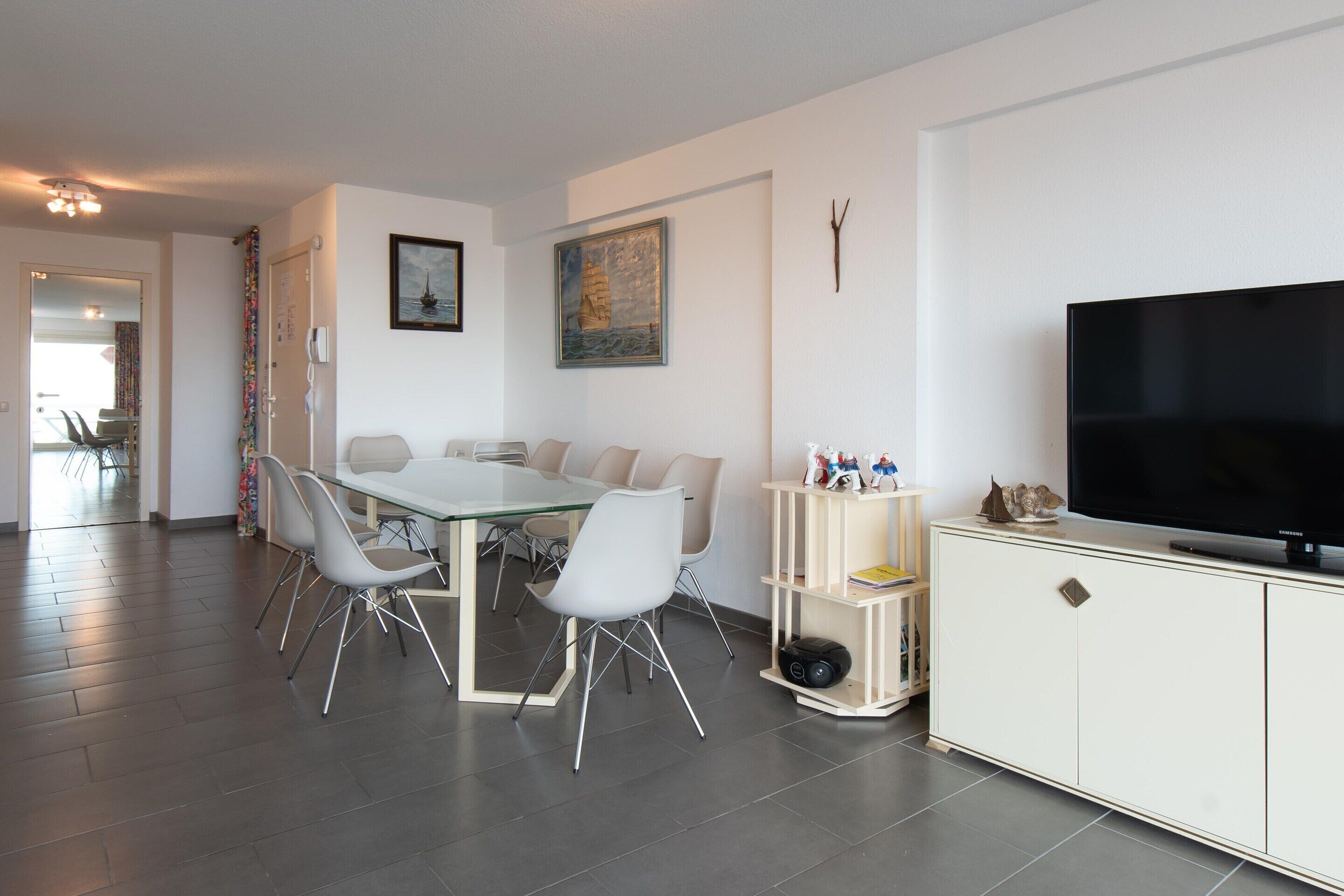 A modern living room with a dining area, a flat-screen TV, and a bookshelf.