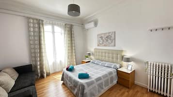 Un dormitorio con cama, mesita de noche, cómoda, radiador y ventana con cortinas.