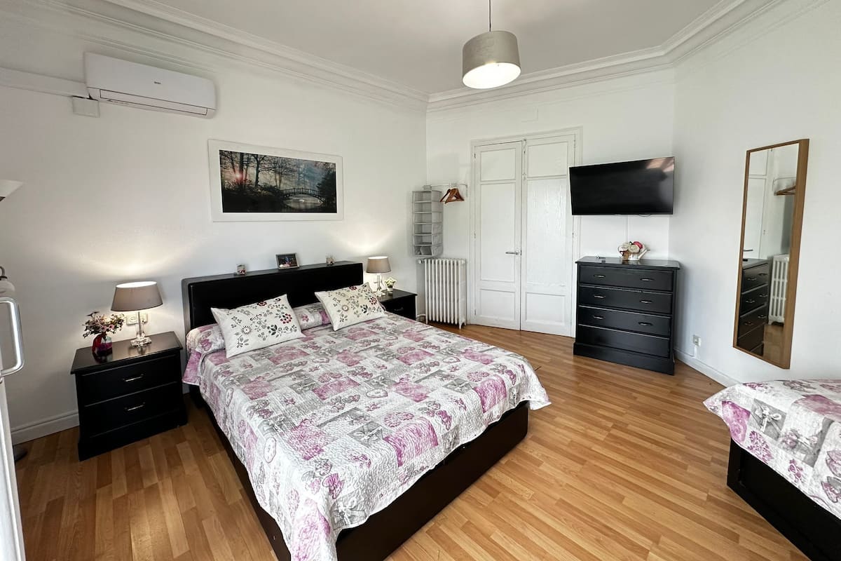 Une chambre à coucher comprenant un lit, des tables de chevet, une commode, un téléviseur, un radiateur et une porte.