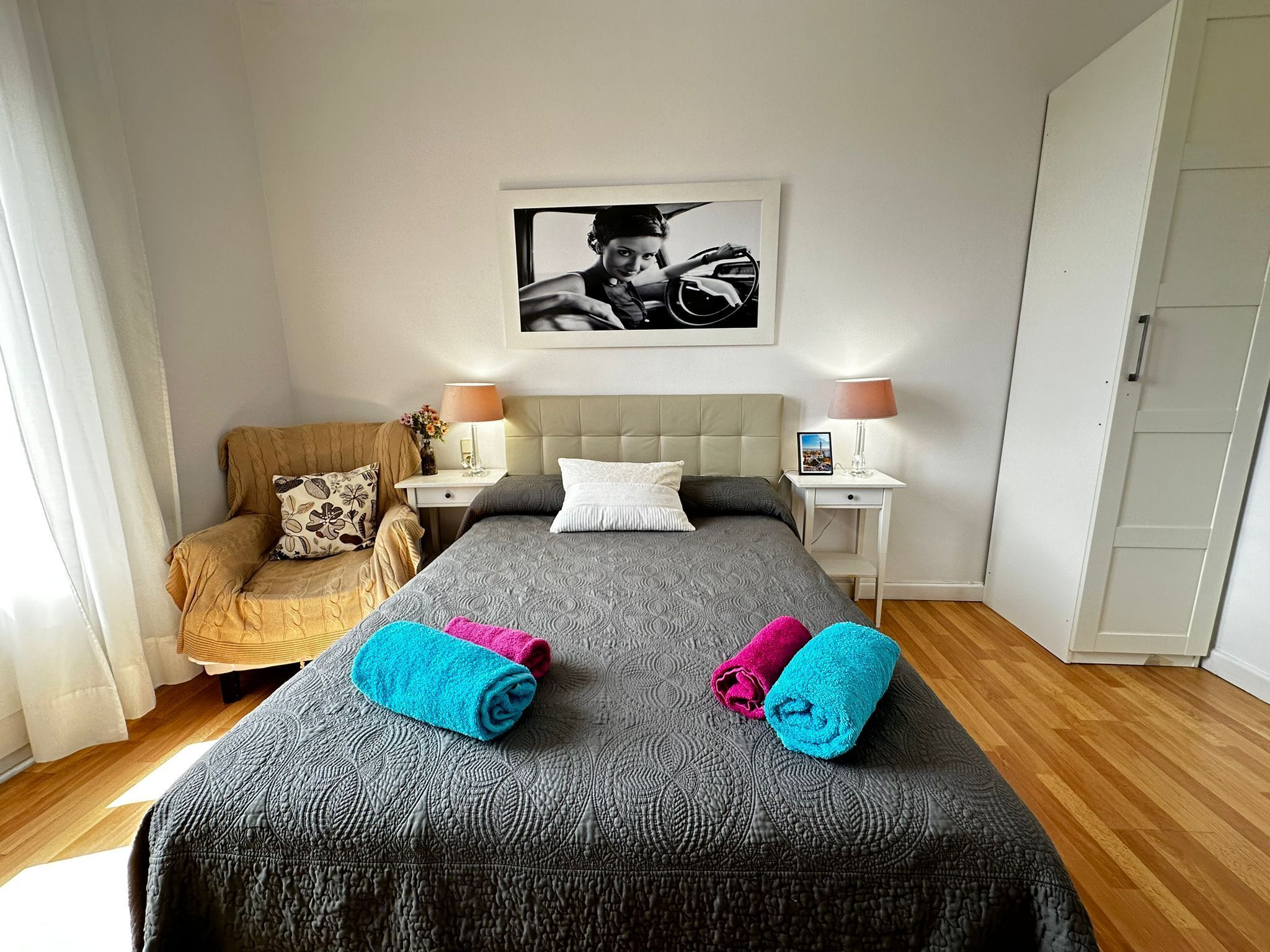 A hotel room with a bed, two nightstands, a chair, and a wardrobe.